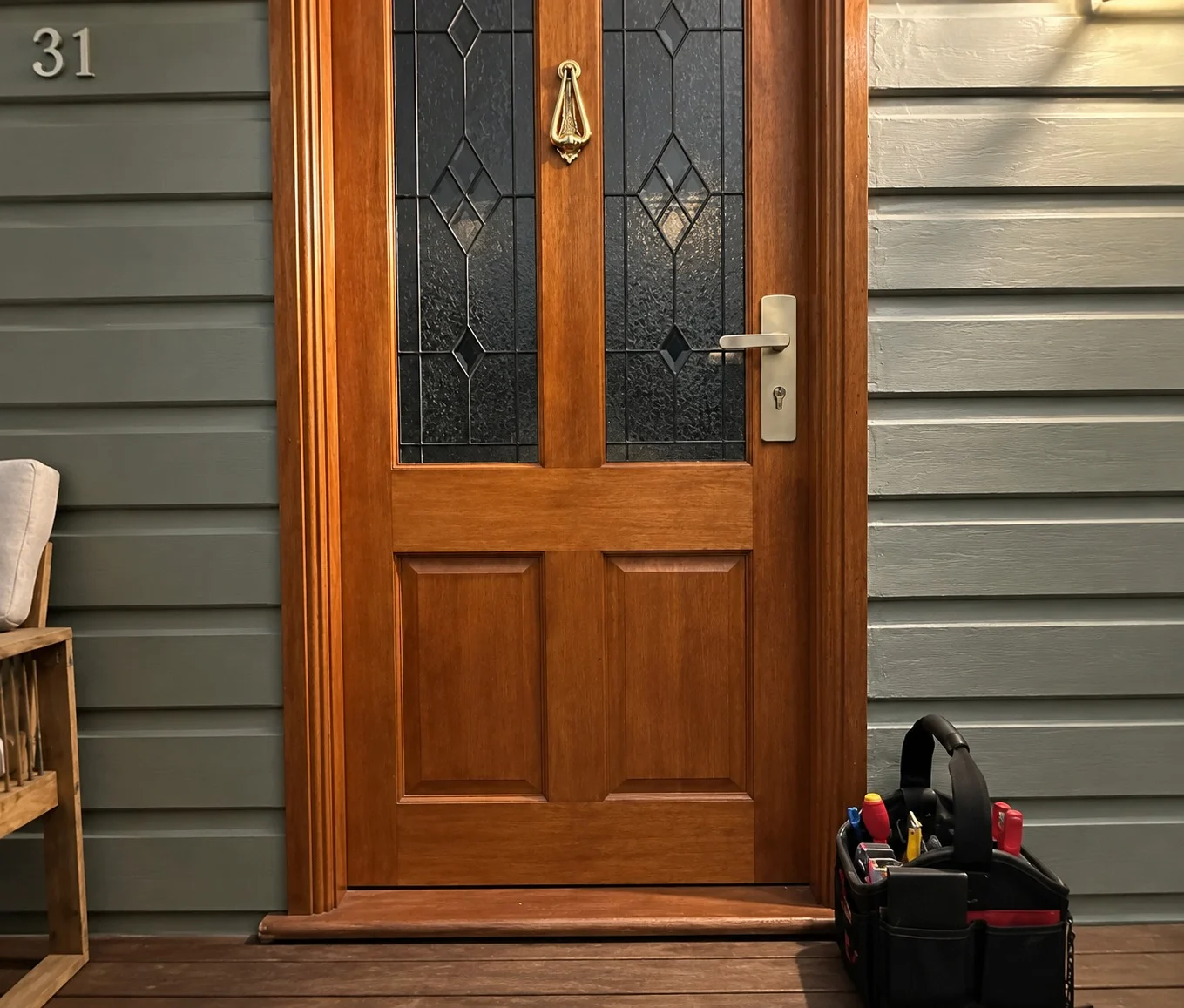 Timber front door with a keyed lever handle and a tool bag on the deck